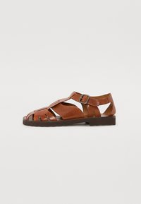 Brune lær sandaler med et åbent design, der har horisontale og vertikale stropper, spænde lukning og en tekstureret gummisål.