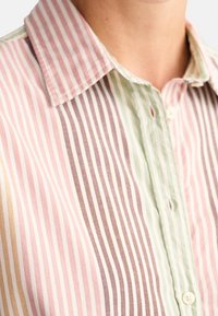 Chemise rayée présentant des lignes verticales en rose, vert, marron et crème, dotée d'un col et d'une fermeture à boutons, fabriquée dans un tissu léger.