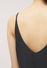 Camisole en tissu noir avec des bretelles fines, présentant un décolleté en V profond au dos. La texture est lisse, mettant en avant un design minimaliste.