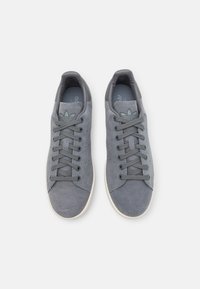 Grå mockaskor med en slät yta, rund tå och platta grå snören. Har subtil branding och en gummisula.