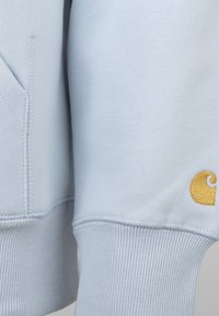 Felpa blu chiaro con polsini e orlo a costine. Presenta una tasca a marsupio e un logo ricamato in oro sulla manica. Tessuto morbido.