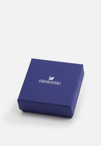 Swarovski šperkovnica, štvorcový tvar, textúrovaný purpurový materiál, vyrazené logo značky v striebre, hladké hrany, kompaktný dizajn.