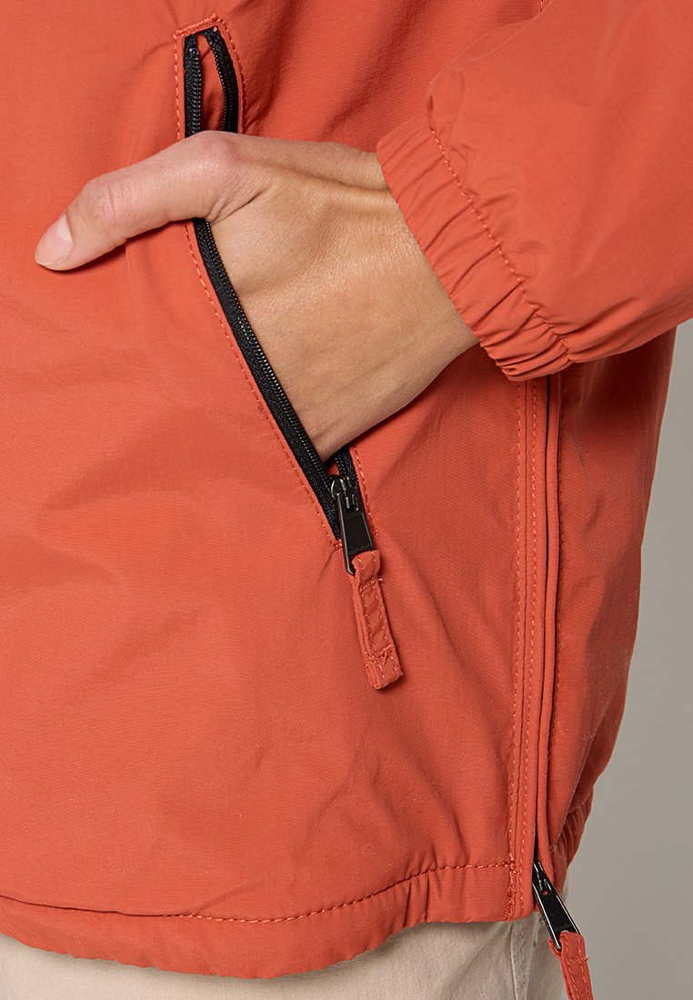 Giacca esterna arancione con tasca con zip e polsini elastici. Il materiale sembra liscio con una leggera lucentezza e una struttura leggera.