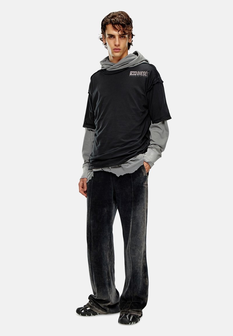 Schwarzes T-Shirt über einem grauen Langarmshirt, kombiniert mit dunkelgrauen Cordhosen. Die Sneaker verfügen über ein strukturiertes schwarzes Design.