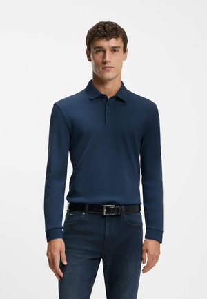 Navy long-sleeve polo shirt with a subtle logo, made of a smooth material. Worn with dark jeans and a black belt featuring a silver buckle.