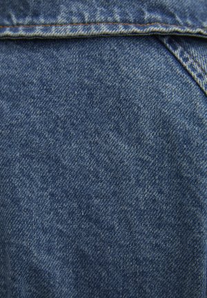 Tissu en denim avec une surface texturée, présentant des tons de bleu et des variations subtiles de couleur, avec des coutures visibles le long des bords.