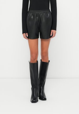 Sorte skinnshorts med elastisk midje, kombinert med elegante svarte knelange støvler med glidelås på siden. Glatt tekstur, tettsittende design.