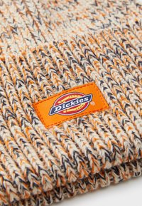 Gorro de malha em laranja, creme e azul-marinho com um padrão texturizado. Apresenta um retângulo laranja com um logotipo na parte da frente.