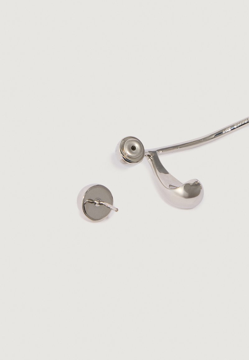 Silberne gebogene Metall-Ohrstecker mit einem kreisförmigen Stecker und einem separaten runden Ohrstecker auf einem schlichten weißen Hintergrund.