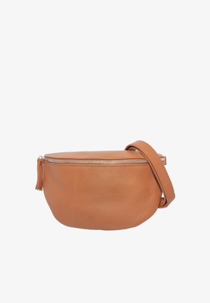 Junge Frau mit schwarzem Langarmoberteil und Lederhose, lächelnd, mit großer brauner Leder-Umhängetasche quer über der Brust.