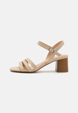 Beige sandalen met bandjes, voorzien van drie horizontale banden en een gespsluiting rond de enkel, met een houten blokhak en een gladde leren afwerking.