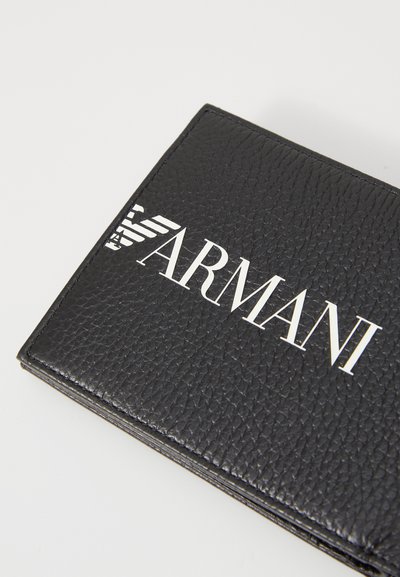 Melnas ādas maks ar teksturētu virsmu. Izceļas ar izteiksmīgu balto "ARMANI" logo un gludu taisnstūra formu.