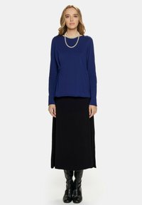 Niebieska bluzka z długim rękawem z marszczeniem, zestawiona z długą czarną spódnicą i czarnymi kozakami do kolan. Perłowy naszyjnik jako akcent.
