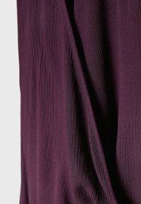 Tissu texturé violet profond avec des plis verticaux subtils et un drapé doux créant des ombres et de la profondeur.