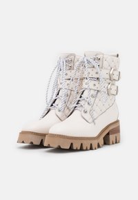 Botas de tobillo con cordones en cuero blanco con acentos acolchados, que presentan cordones de cuerda y hebillas. Suela de plataforma marrón gruesa con surcos distintivos.