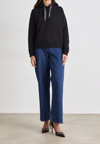 Black hooded sweatshirt with contrasting drawstrings, paired with wide-leg blue denim jeans and black heeled shoes featuring gold accents.