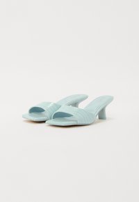 Mule con tacco verde menta, con texture a coccodrillo, design open-toe e un tacco a blocco modesto. Presentano larghe fascette sopra il piede.