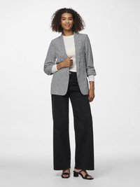 Fekete-fehér houndstooth mintás blézer, egy gombos záródással, világos felsővel, széles lábú fekete nadrággal és fekete magassarkú szandálokkal párosítva.