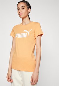 Oranžové bavlnené tričko s krátkym rukávom, na prednej strane s bielym logom "PUMA" a siluetou skáčuceho pumu. Hladká textúra.