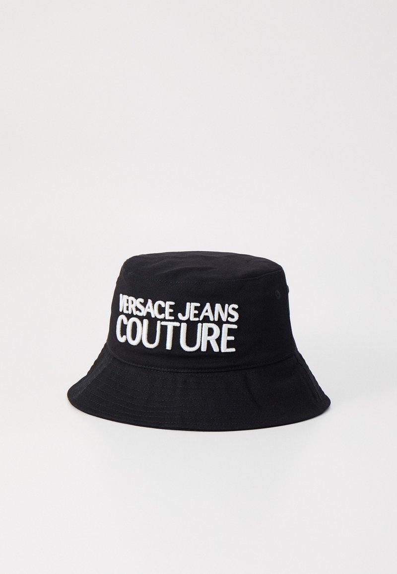 Melnā auduma sieta cepure ar uzšūtu balto "VERSACE JEANS COUTURE" logo priekšpusē. Iezīmē plašu, uz leju slīpo malu.