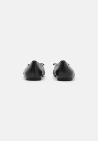 Bailarinas de cuero negro con un diseño elegante, punta redondeada y costuras mínimas. Presentan un pequeño tacón y lazos de tela para el cierre.