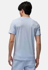 Maglietta in cotone blu chiaro con maniche corte, scollatura rotonda e una texture liscia, mostrata di spalle, abbinata a pantaloni blu chiaro.