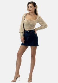 Top beige arricciato a maniche lunghe con scollo quadrato, abbinato a una mini gonna in denim blu scuro con orlo sfilacciato. Sandali con tacco trasparente.