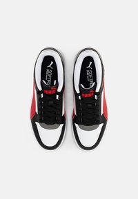 Baskets noires, blanches et rouges avec une texture lisse, dotées d'un système de laçage, d'une languette rembourrée et de bandes latérales contrastées.