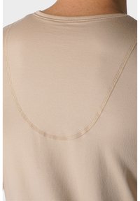 Beżowy t-shirt o gładkiej fakturze, okrągłym dekolcie i subtelnych detalach ściegów wzdłuż ramion i dekoltu.