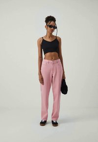 Jeans rosa de cintura alta, con un ajuste ligeramente holgado, combinados con un top de tirantes negro corto. Unas gafas de sol negras y un pequeño bolso negro completan el conjunto.
