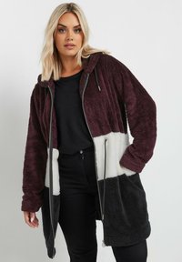 Chaqueta con capucha de forro polar que presenta un diseño a bloques de color en burdeos, blanco y negro. Manga larga con dobladillos ajustados, cierre de cremallera y bolsillos laterales.
