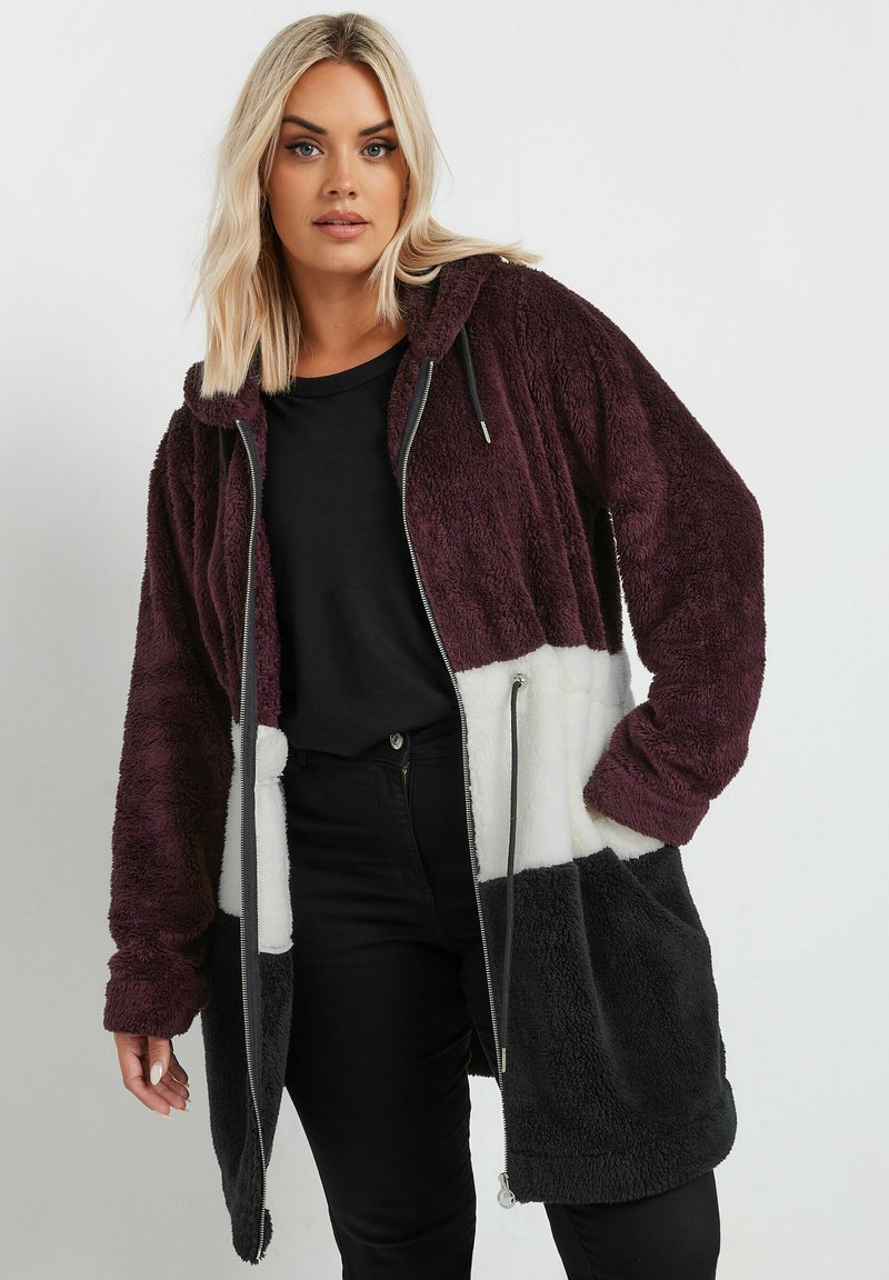 Chaqueta con capucha de forro polar que presenta un diseño a bloques de color en burdeos, blanco y negro. Manga larga con dobladillos ajustados, cierre de cremallera y bolsillos laterales.