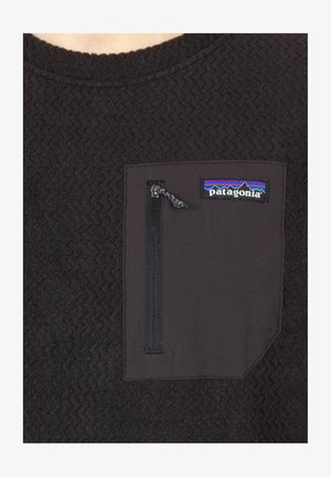 Tumši pelēks vilnas pullovers ar teksturētu virsmu, aprīkots ar rāvējslēdzēja krūšu kabatu un Patagonia logo zilā, purpura un melnā krāsā.