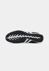 Black and white Adidas sneaker sole with grooved tread pattern and iconic three stripes visible on the side.