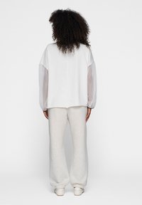 Hvid top med gennemskinnelige pufærmer, parret med beige sweatpants. Glat tekstur, afslappet pasform og elastiske manchetter på bukserne.