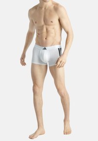 Vit bomullsbrief med svart tre-stripesdesign på midjebandet. Tätt sittande, slät textur och stödjande frontficka.