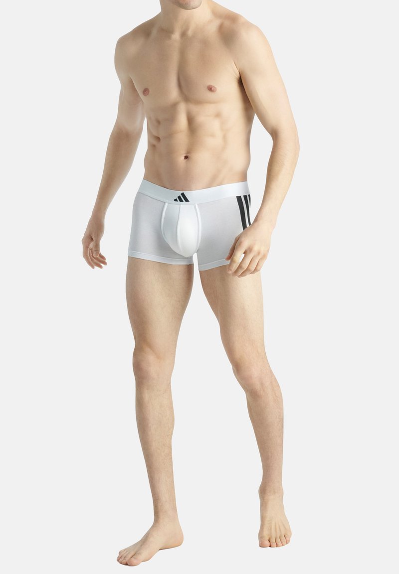 Vit bomullsbrief med svart tre-stripesdesign på midjebandet. Tätt sittande, slät textur och stödjande frontficka.