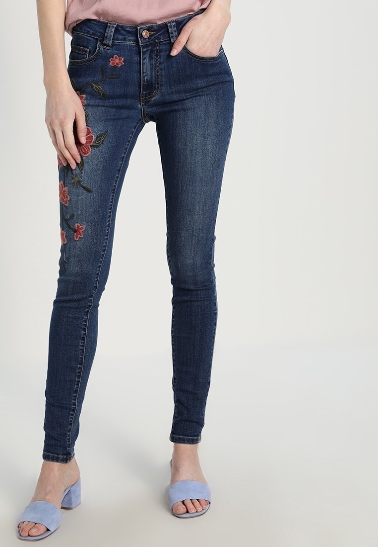Tmavě modré úzké džíny s květinovou výšivkou na levé noze. Vyrobené z denimu, s pasem ve střední výšce a pětikusovým kapsovým designem.