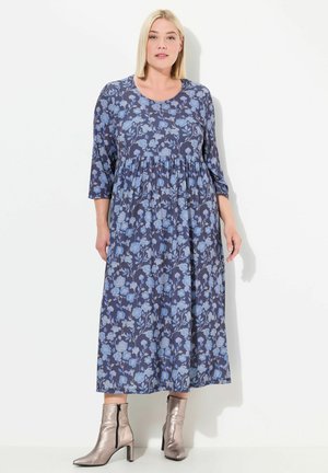 Robe maxi à imprimé floral en bleu marine avec des fleurs bleu clair, décolleté rond, manches trois-quarts et taille froncée. Bottes cheville argentées.