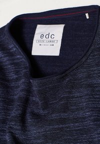 T-shirt in jersey blu navy con scollo rotondo, tessuto strutturato, e un'etichetta con la scritta "edc TAGLIA-GRANDE" con un accento rosso sul colletto interno.
