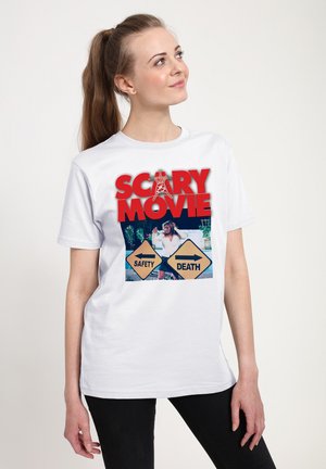 T-shirt en coton blanc avec un motif graphique comprenant le texte "SCARY MOVIE" en rouge et une image de deux panneaux directionnels étiquetés "SÉCURITÉ" et "MORT."