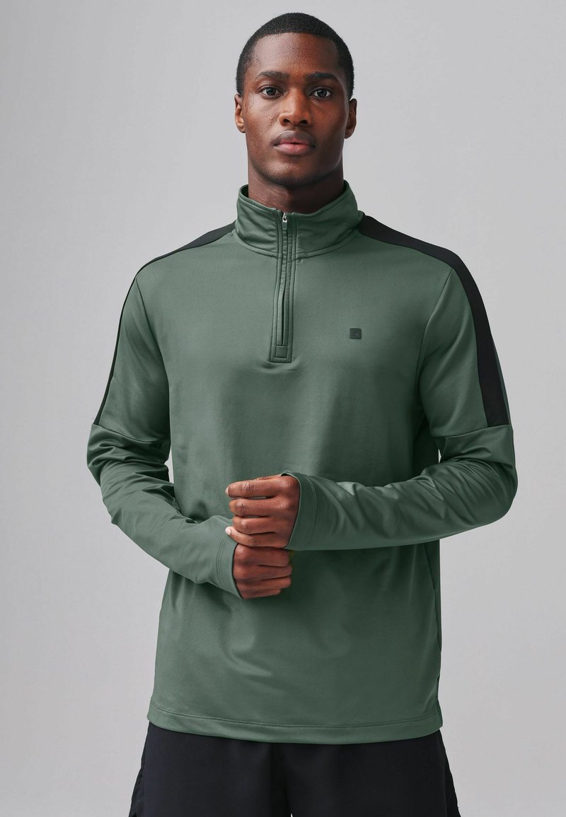 Camiseta deportiva de manga larga verde con un cuello tipo quarter-zip, acentos en negro contrastante en los hombros y un diseño ajustado, hecha de tela suave.