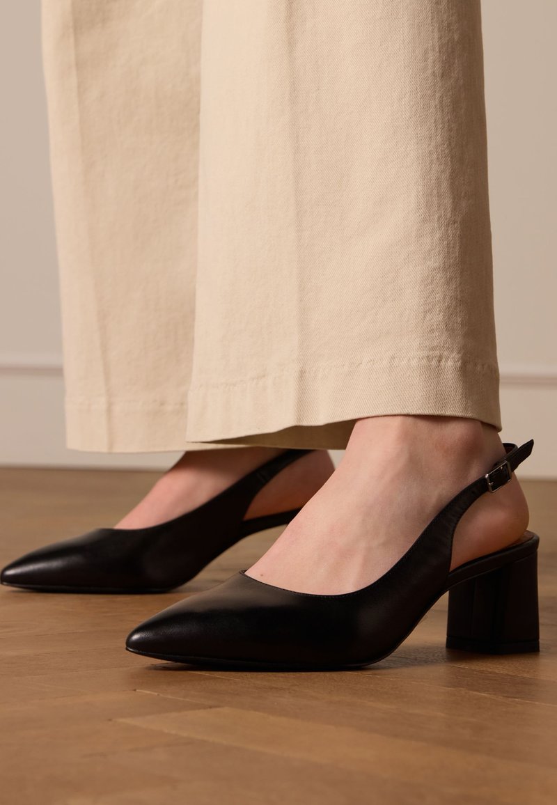 Zwarte slingback hakken met een spitse neus, glanzend leren materiaal, blokhak en verstelbare enkelband. Gecombineerd met crèmekleurige brede broek.