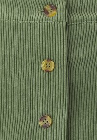 Tissu vert côtelé avec trois boutons ronds aux tons multiples. Surface texturée mettant en valeur des lignes verticales et un léger éclat.