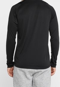 Pitkähihaisessa mustassa urheilupaidassa on sileä tekstuuri ja raglan-hihat, joita on yhdistetty vaaleanharmaisiin verkkareihin.