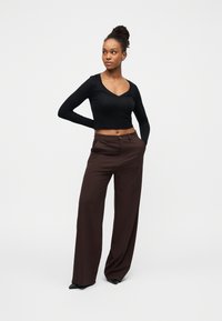 Μαύρο crop top με μακριά μανίκια και V-λαιμόκοψη· συνδυασμένο με καφέ φαρδιά παντελόνια με ψηλή μέση· απαλό ύφασμα· μινιμαλιστικός σχεδιασμός· εφαρμοστή σιλουέτα.