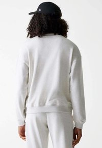 Felpa grigia con una vestibilità comoda, polsini e orlo a costine. Il tessuto appare morbido, texturizzato e leggermente felpato. Abbinata a pantaloni jogger coordinati.