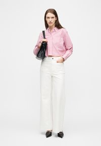 Γυναίκα με cropped πουκάμισο ροζ και άσπρες ρίγες, άσπρο παντελόνι με φαρδιά μπατζάκια, μαύρα μυτερά παπούτσια, κρατώντας μαύρη τσάντα στον ώμο.