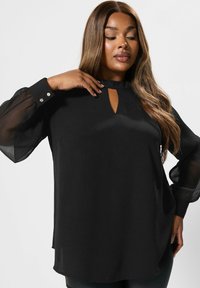 Blusa nera con maniche lunghe trasparenti, scollatura a chiave e dettagli con bottoni ai polsini. Tessuto liscio e vestibilità comoda.