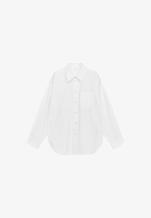 Witte oversized blouse met lange mouwen, spitse kraag, knoopsluiting aan de voorkant en een enkele borstzak, weergegeven tegen een eenvoudige achtergrond.